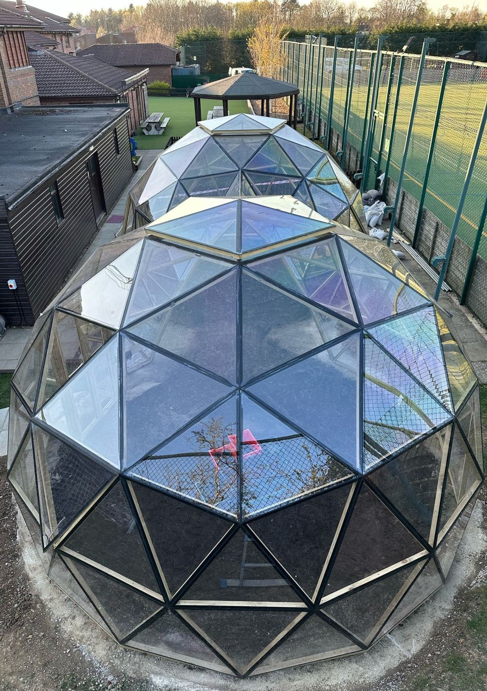 The linked dome pair from above, school sports courts behind