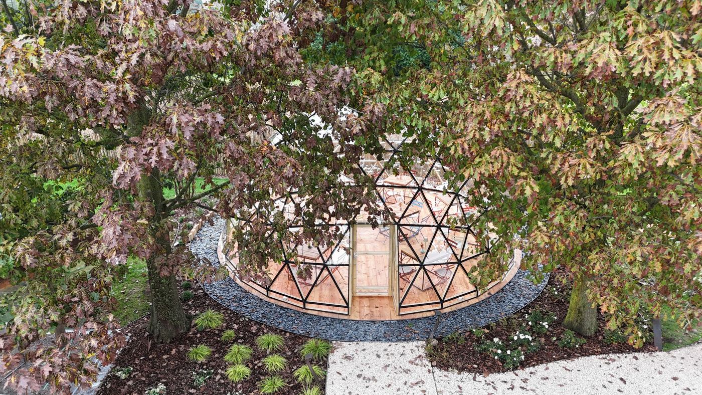 Aerial view of the 8m fully glazed geodesic timber dome among mature garden trees at Il Gallese farm, Scorzè